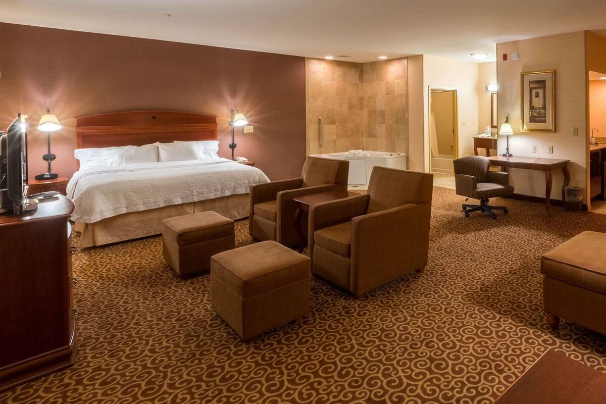 Una habitación de hotel con una cama, dos sillones, un sofá, un escritorio, una silla y un baño.