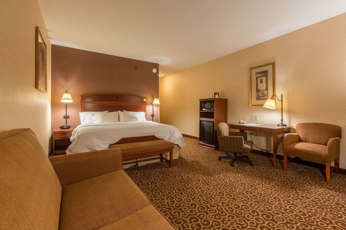 A hotel room with a bed, desk, office chair, and a sofa.