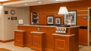 A reception desk with a clock, framed pictures, and a welcome sign. - Hampton Inn Goshen (Goshen)