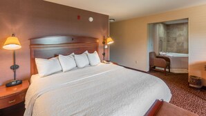 A hotel room with a large bed, two bedside lamps, a chair, and a bathroom with a bathtub and shower. - Hampton Inn Goshen (Goshen)