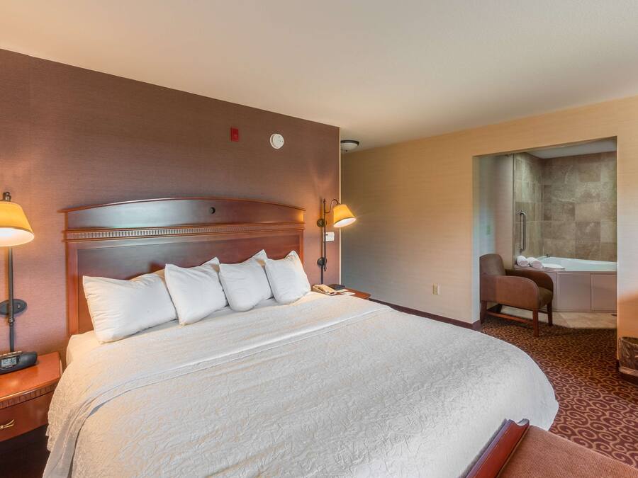 Una habitación de hotel con una cama grande, dos lámparas de noche, una silla y un baño con bañera y ducha.