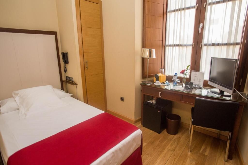Habitación de hotel con cama, escritorio, silla, televisor y refrigerador pequeño.