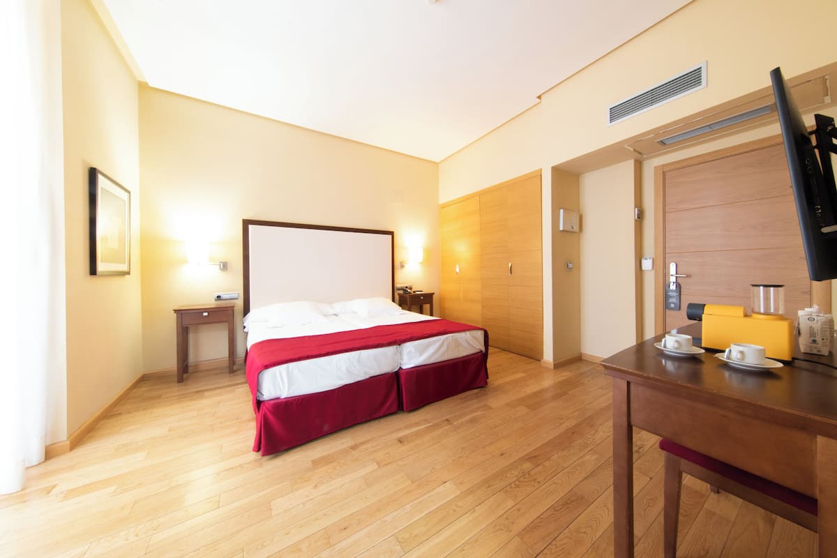 A hotel room with a bed, bedside tables, a desk with a chair, a television, and a wooden wardrobe.