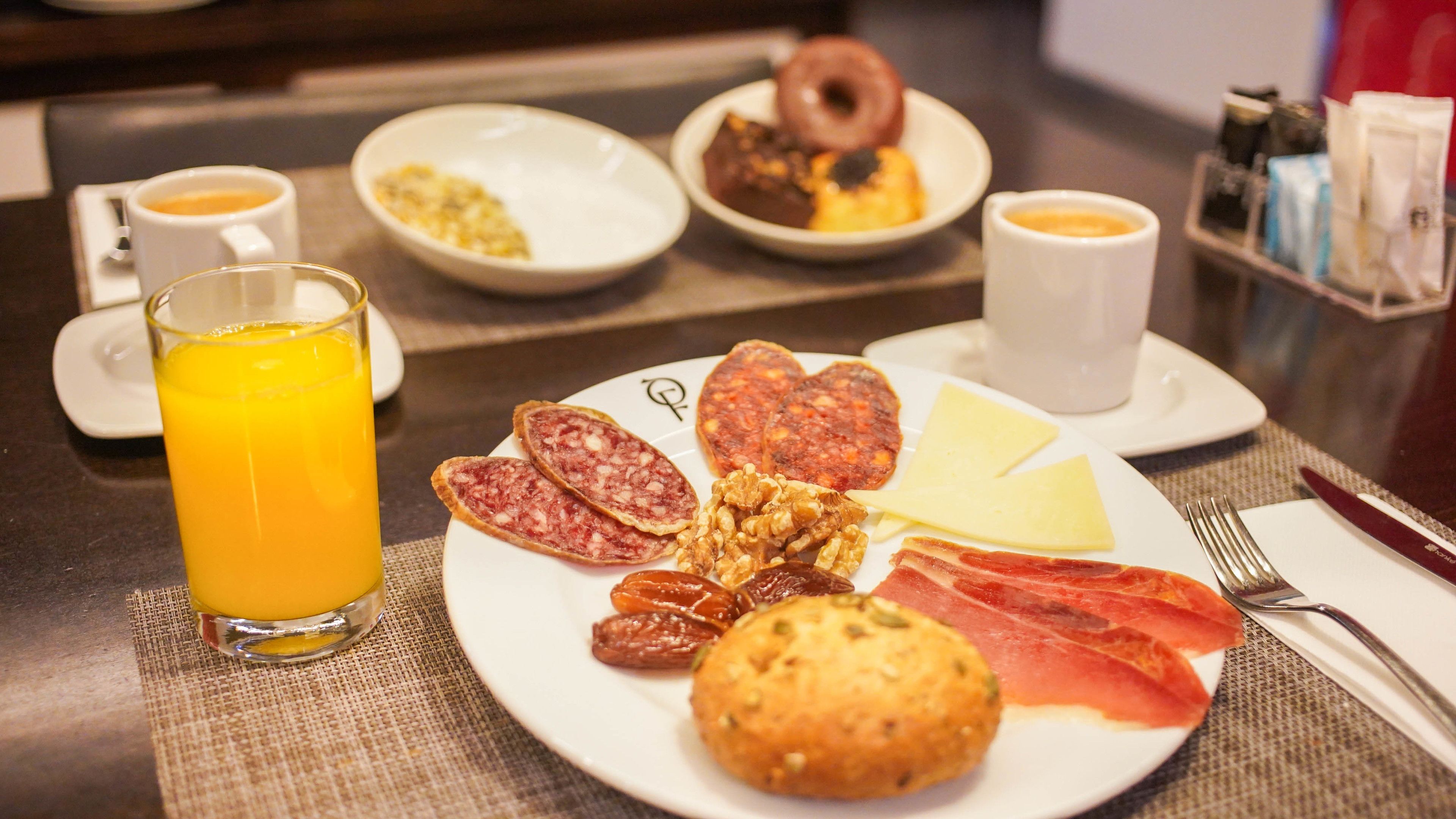 Un desayuno con un plato de comida, un vaso de zumo de naranja y dos tazas de café.