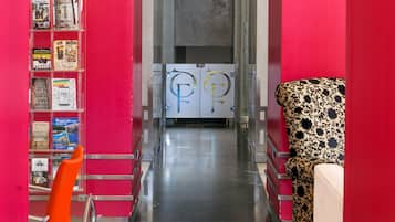 Un pasillo con paredes rojas, una puerta de cristal, un sillón estampado y un mueble para revistas.