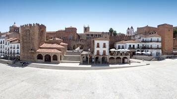 Una plaza histórica con edificios de piedra, una fuente central y una estructura similar a un castillo.