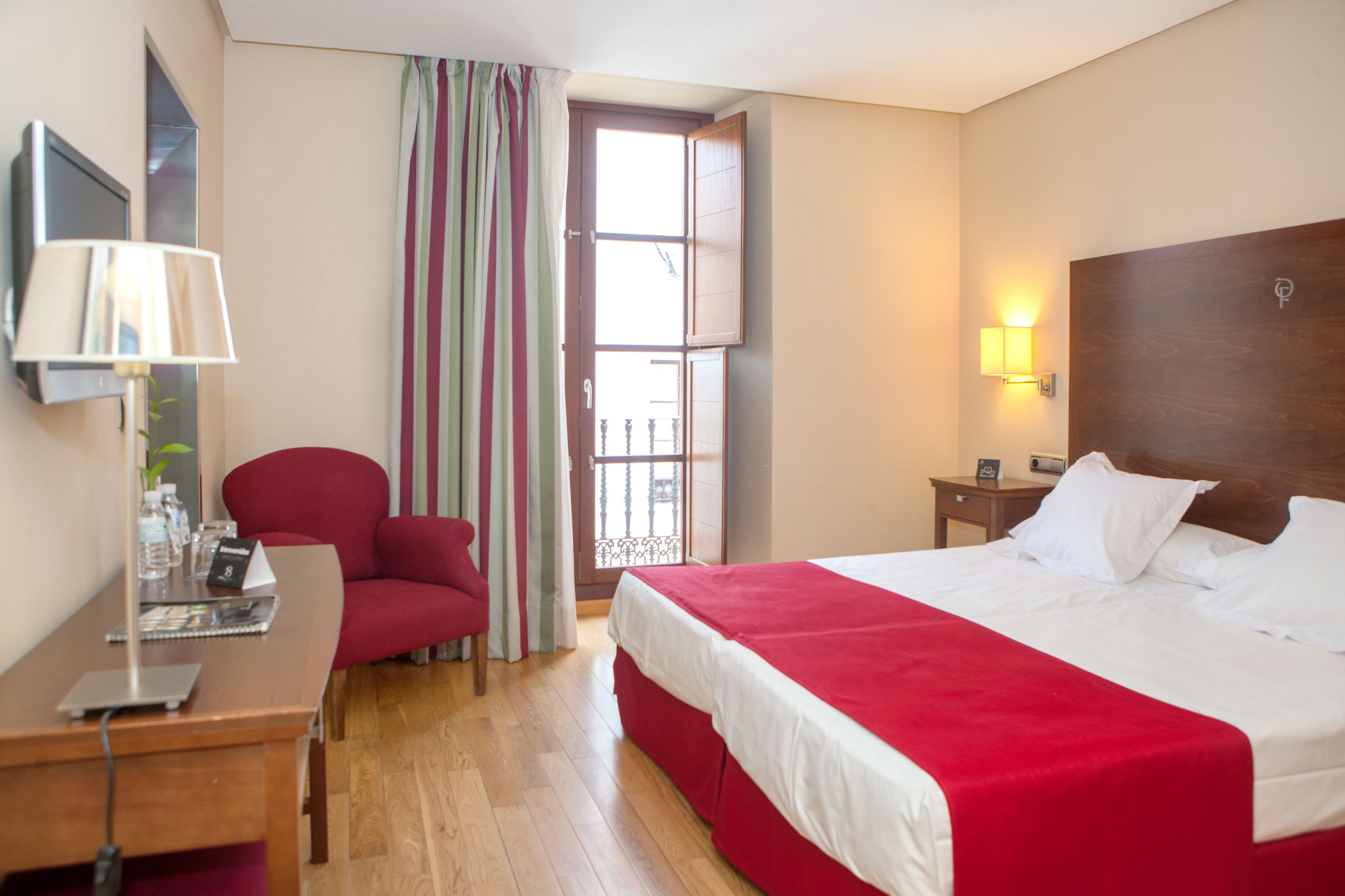 Een hotelkamer met een bed, bureau, stoel en raam met gordijnen.