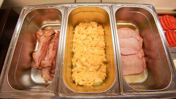 A stainless steel buffet with three compartments containing bacon, scrambled eggs, and sliced ham.