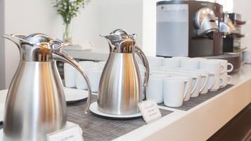 A coffee station with two silver coffee pots and several white coffee cups on a counter.