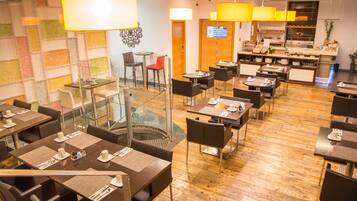 Un restaurante con varias mesas y sillas, una pared de vidrio y una zona de cocina al fondo.