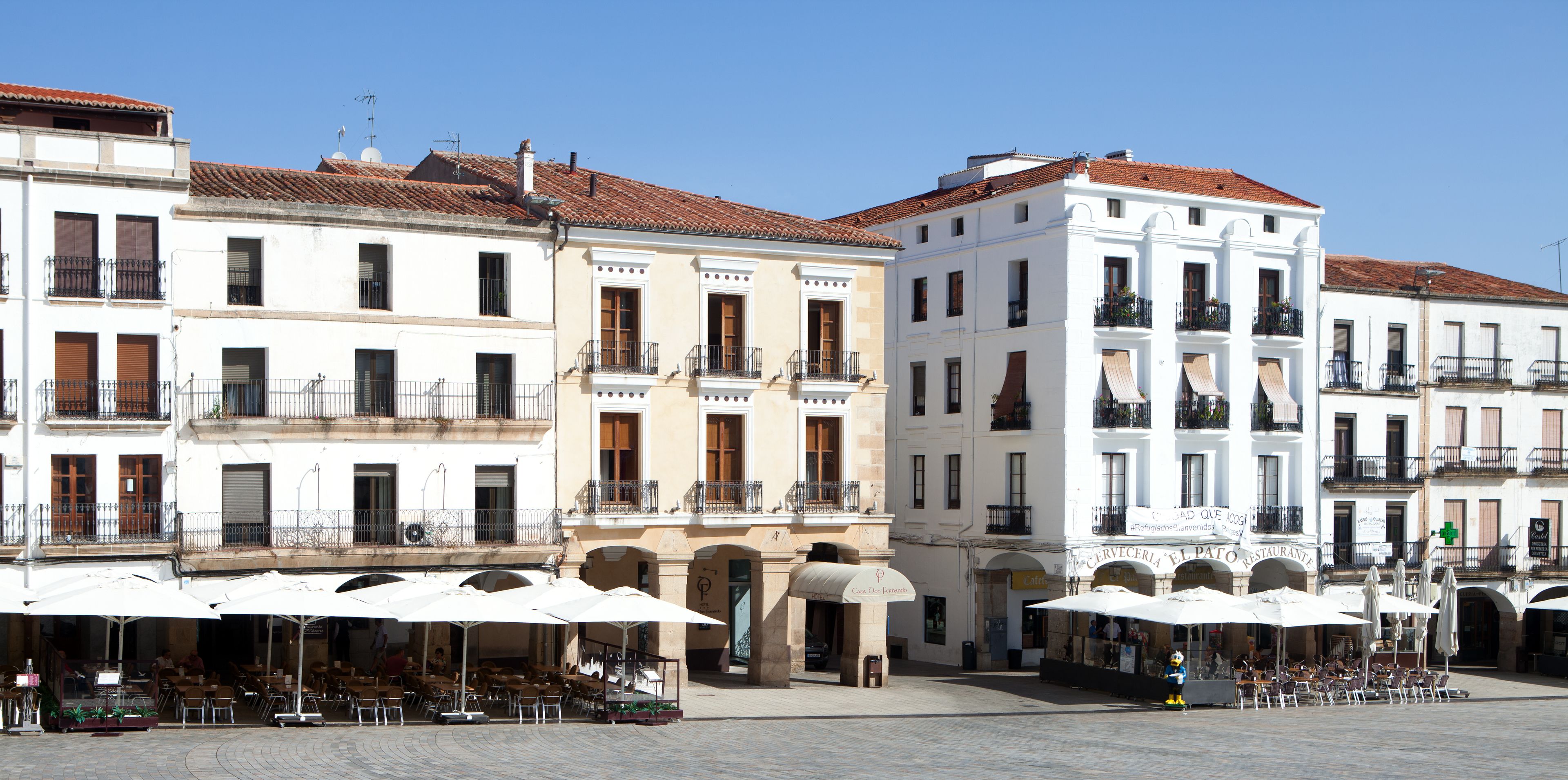 Un espacio cuadrado con mesas al aire libre, edificios blancos y un letrero de restaurante.