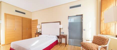 Habitación de hotel con cama, una silla, escritorio y armario.