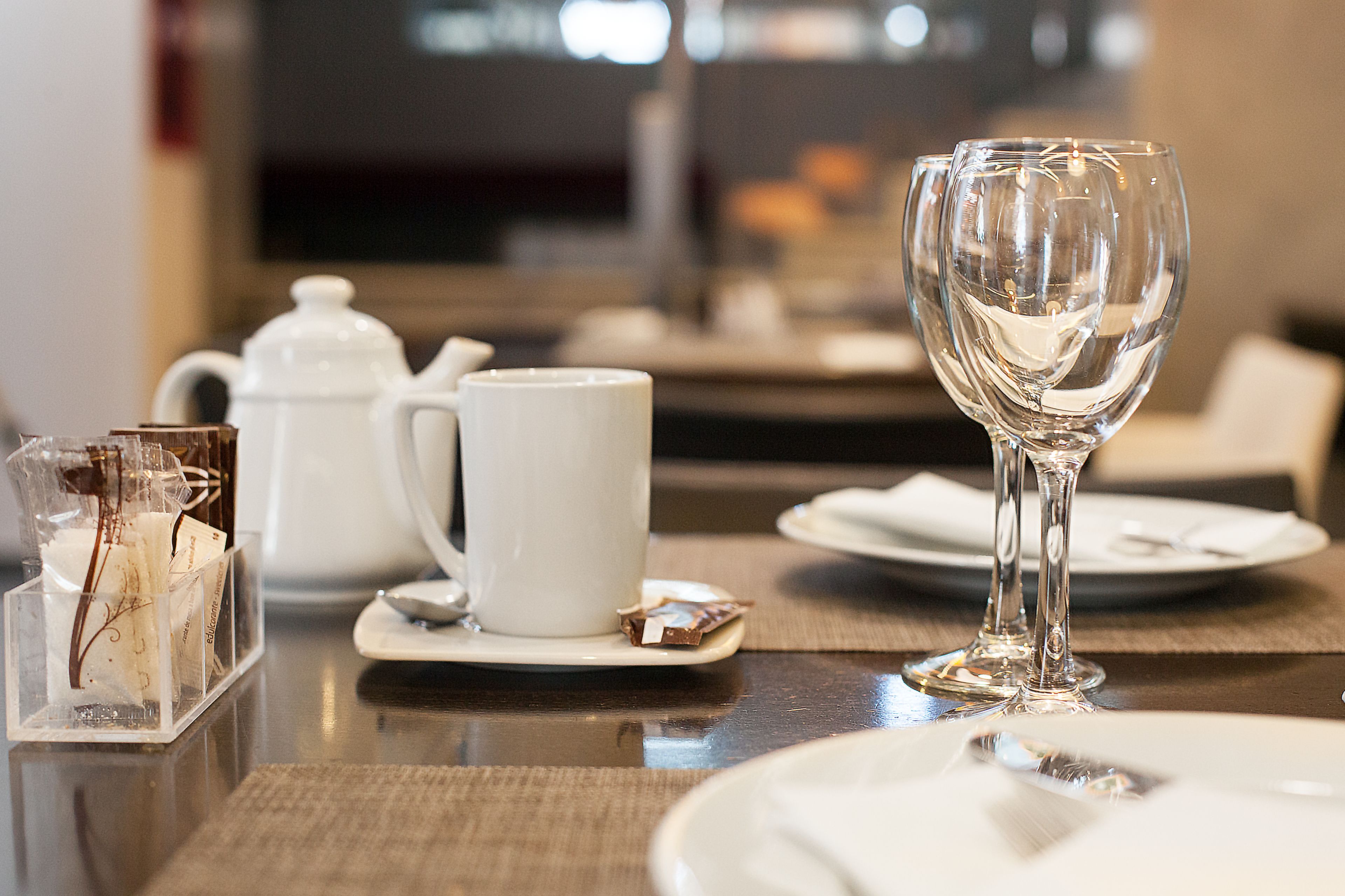 Een eettafel met een witte theepot, een witte kop, een glas en een glazen houder met theezakjes.