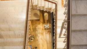 Une vue en miroir du hall d’un hôtel, avec un comptoir d’accueil en bois, un arrangement floral et un sol en marbre.
