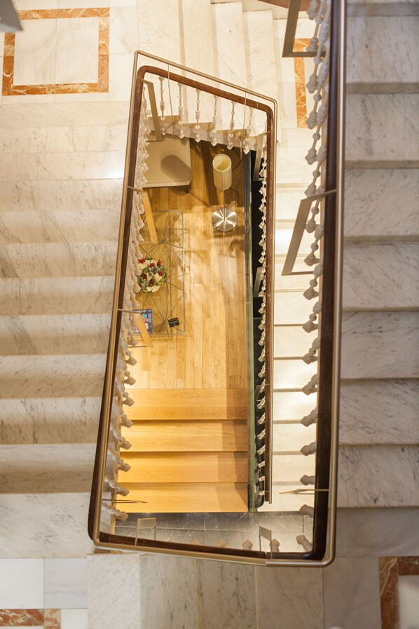 A mirrored view of a hotel lobby with a wooden reception desk, a flower arrangement, and a marble floor.