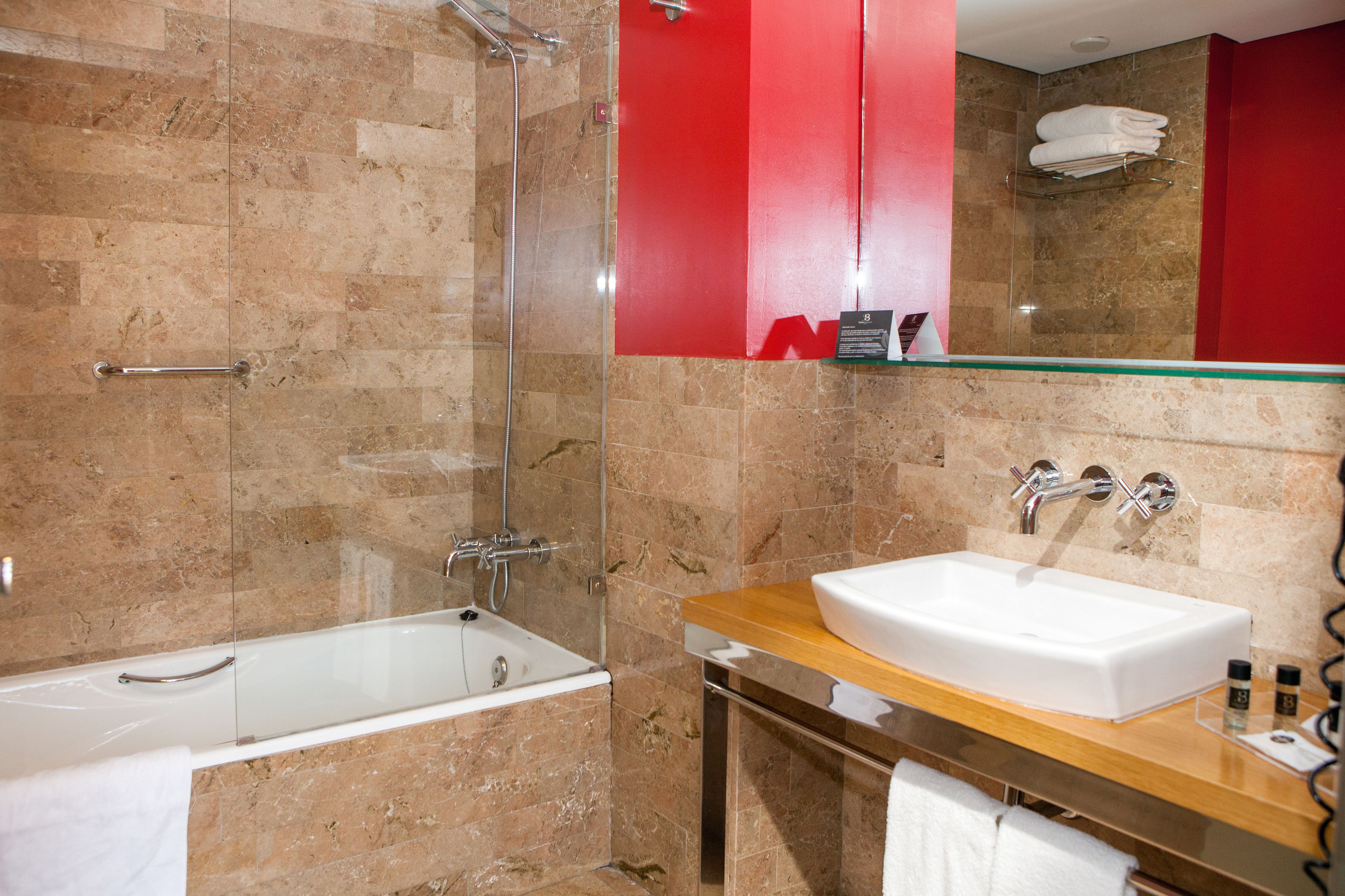 A modern bathroom with a glass-enclosed shower, a white bathtub, and a wooden vanity with a sink.