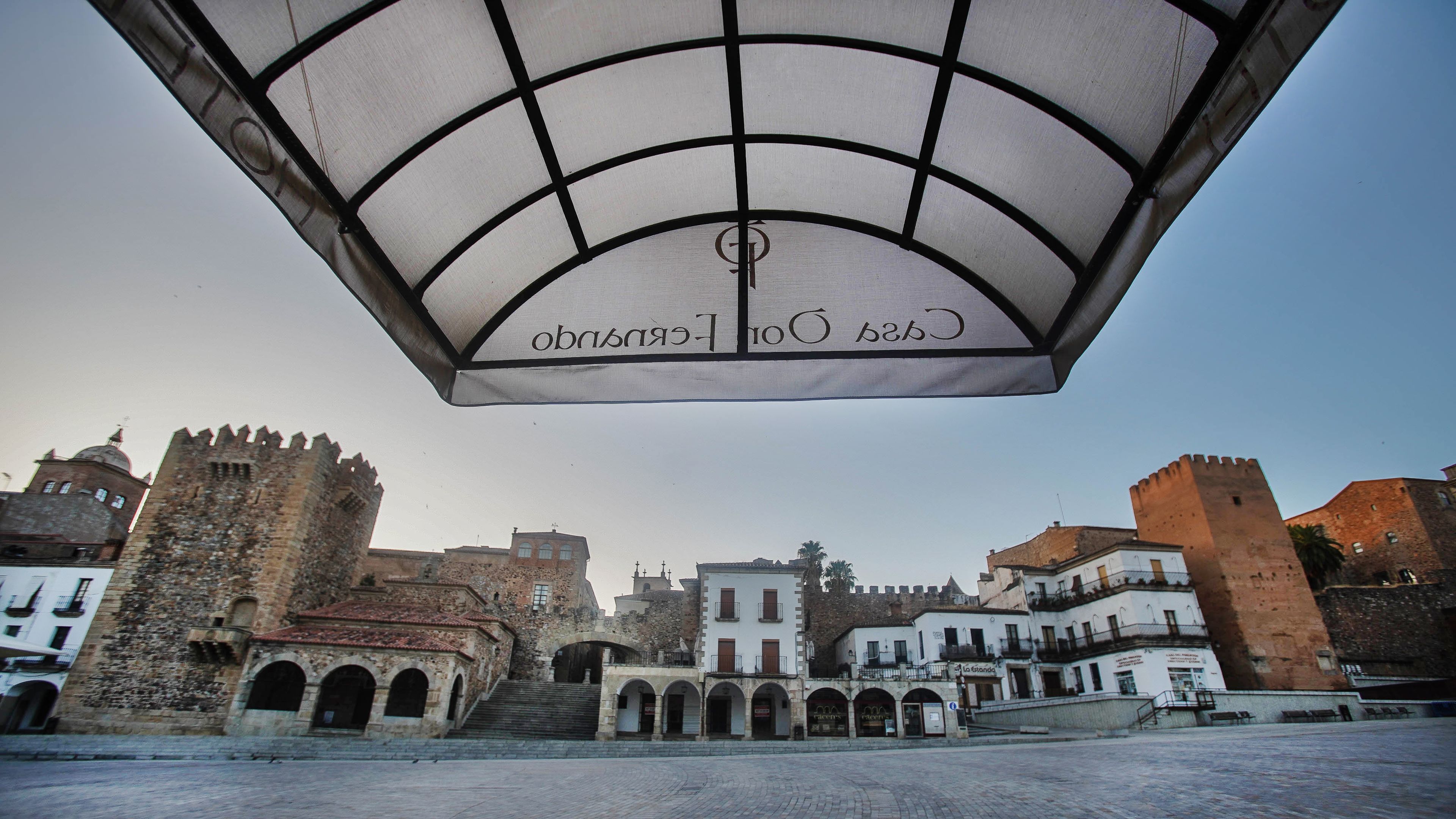 Una plaza histórica con un castillo destacado, una galería techada y edificios tradicionales.