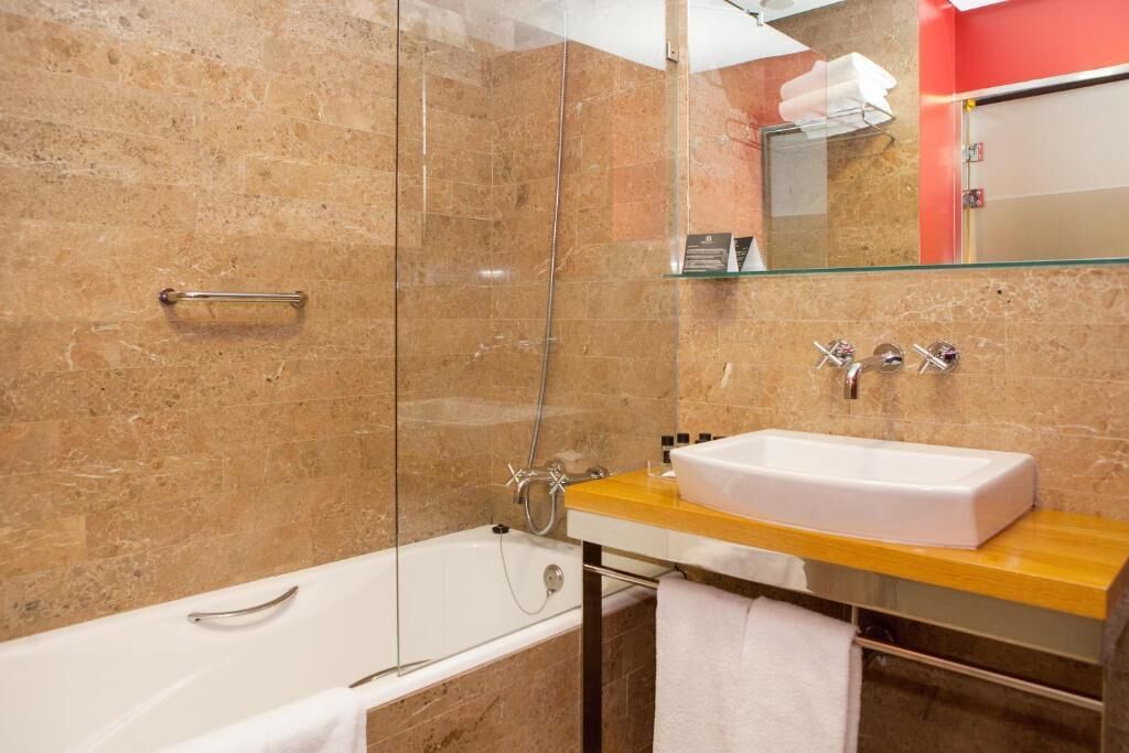 A modern bathroom with a glass-enclosed shower, a white bathtub, and a wooden vanity with a sink.