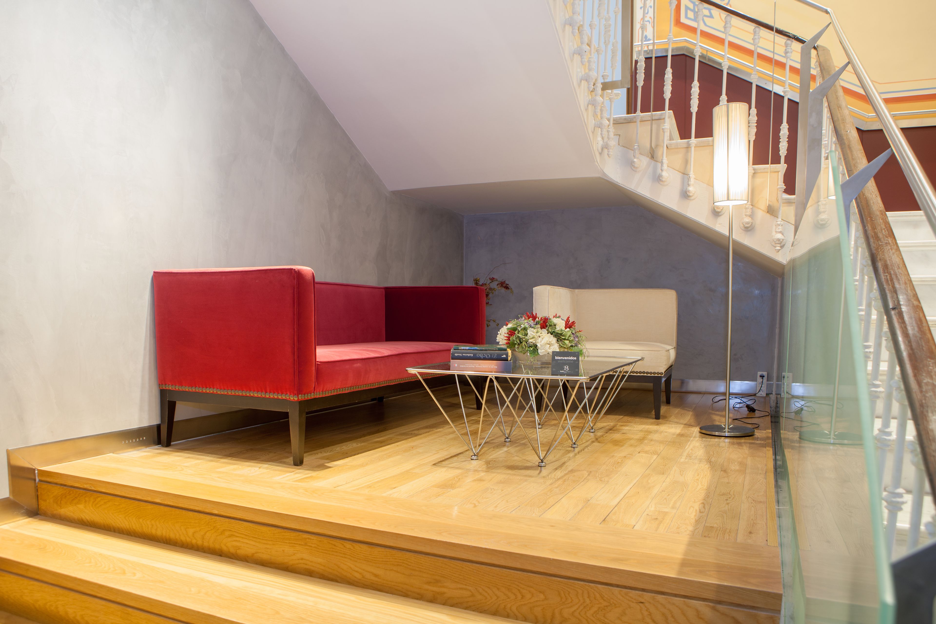 A modern living room with a red sofa, a white armchair, and a glass coffee table.