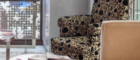 Una sala moderna con un sillón estampado, un sofá color beige y una mesita redonda con libros.