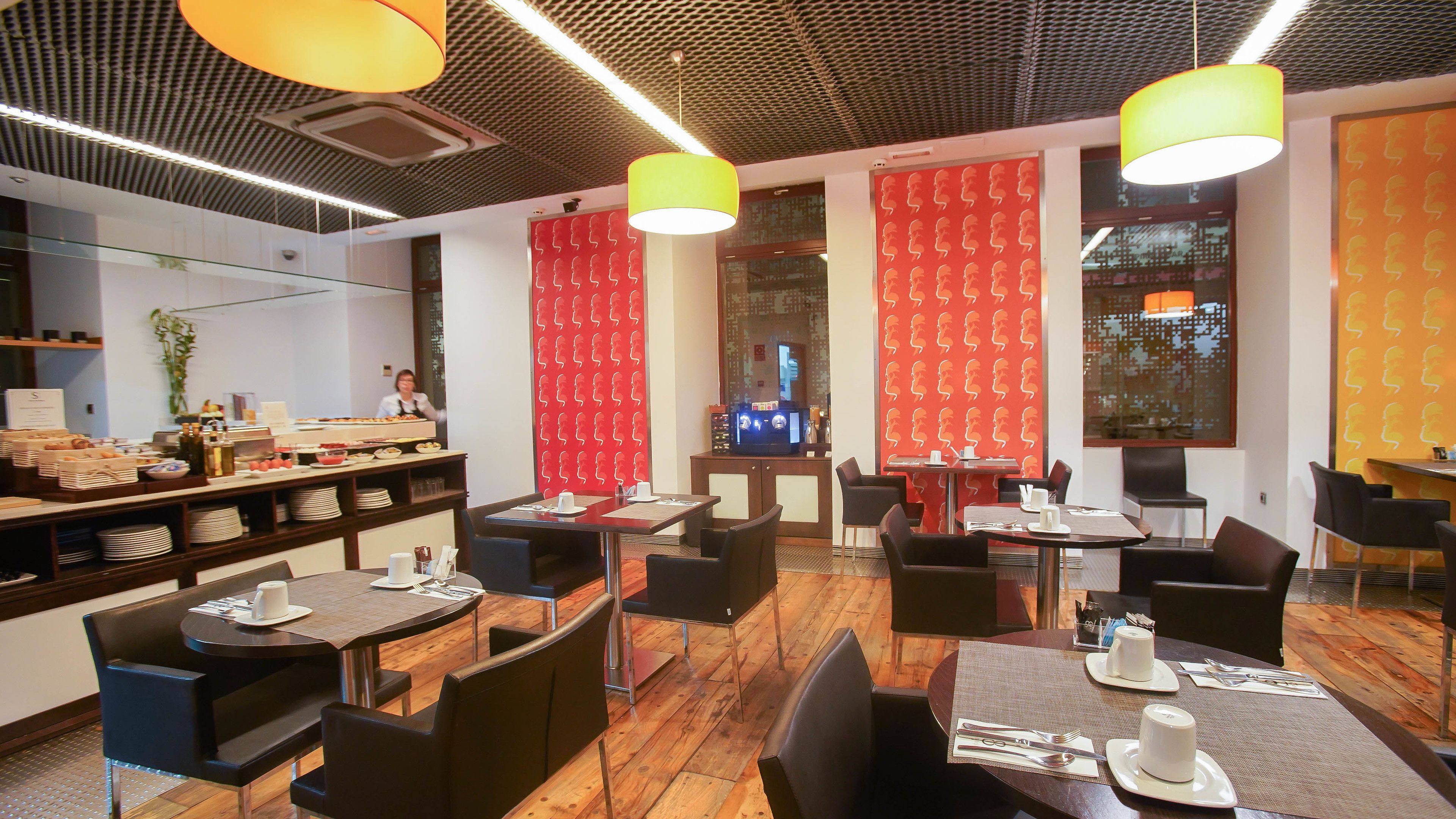 Un interior de restaurante moderno con suelo de madera, sillas negras y marrones, y lámparas colgantes amarillas.