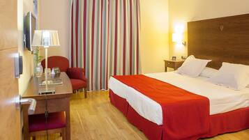 A hotel room with a bed, a desk, a chair, a lamp, a nightstand, and a striped curtain.