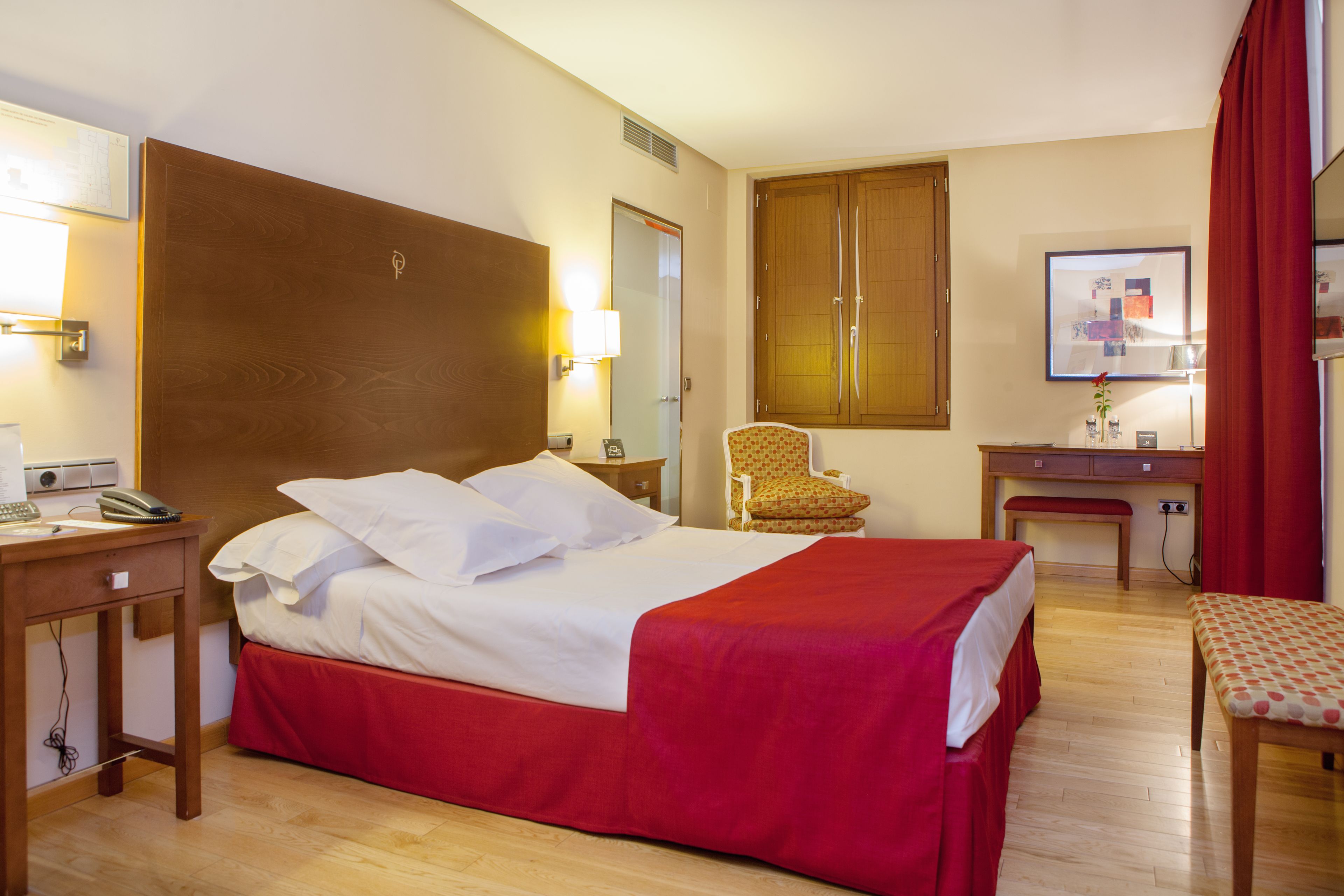 Una habitación de hotel con una cama de madera, un escritorio con una silla, una mesita pequeña y un banco.