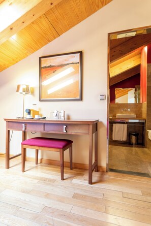 A wooden desk with drawers, a bench, a lamp, and a framed painting on the wall.