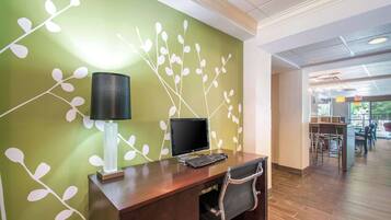 Un mostrador de recepción con una computadora, una lámpara y una silla en un vestíbulo con pared verde y piso de madera.