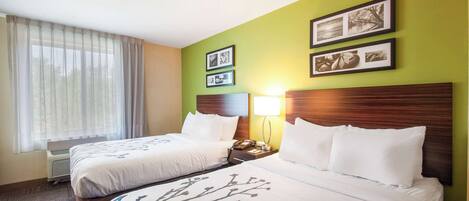 A hotel room with two beds, a large window with sheer curtains, a wall-mounted air conditioner, and framed pictures on the wall.