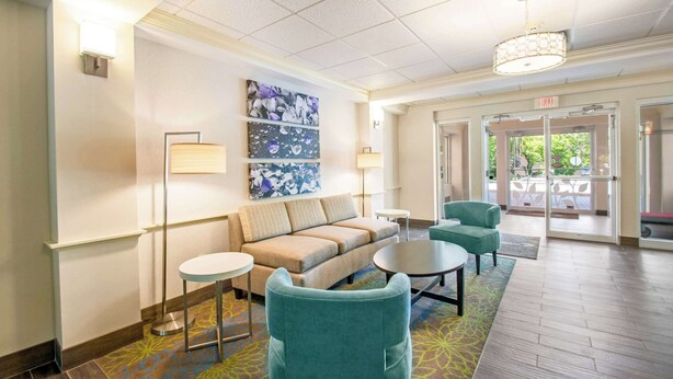 A lobby with a sofa, two armchairs, a coffee table, and a floor lamp. There is a painting on the wall and a door leading outside. - Sleep Inn & Suites Dover University Area (Dover)