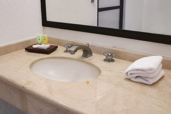 A bathroom sink with a mirror above it, a towel stacked on the right, and a soap dispenser on the left.