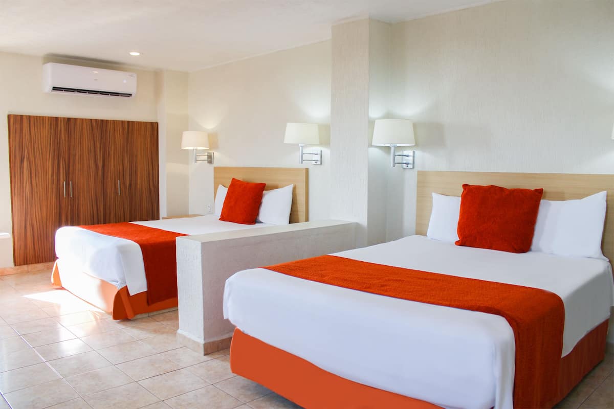 Une chambre d’hôtel avec deux lits, chacun agrémenté de draps blancs et de touches de couleur orange, ainsi qu’une armoire en bois.