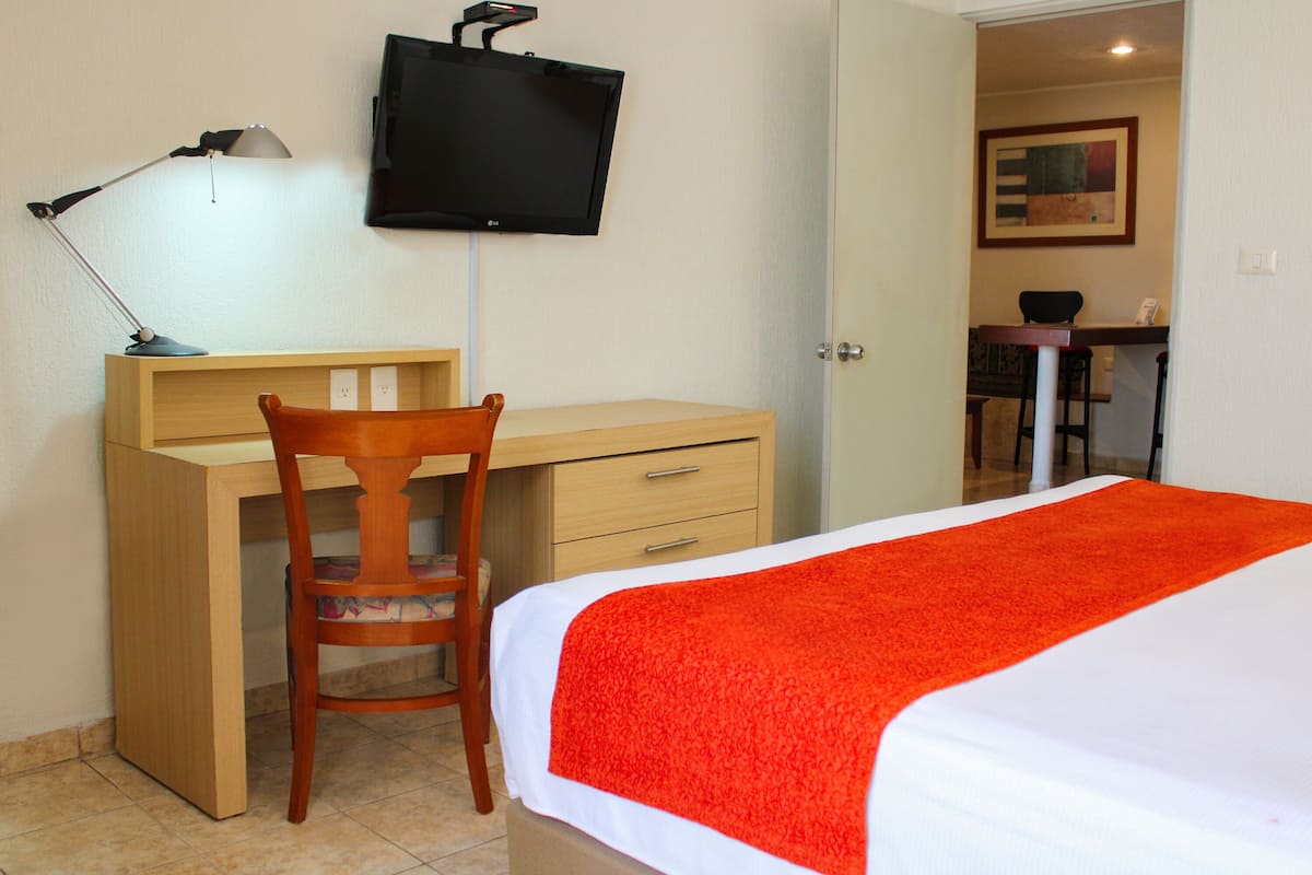 Une chambre d’hôtel avec un lit, un bureau, une chaise, une télévision et un tableau au mur.