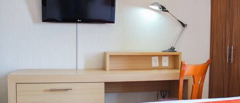 Une chambre à coucher avec un lit, un bureau et une chaise, un téléviseur fixé au mur et une lampe.
