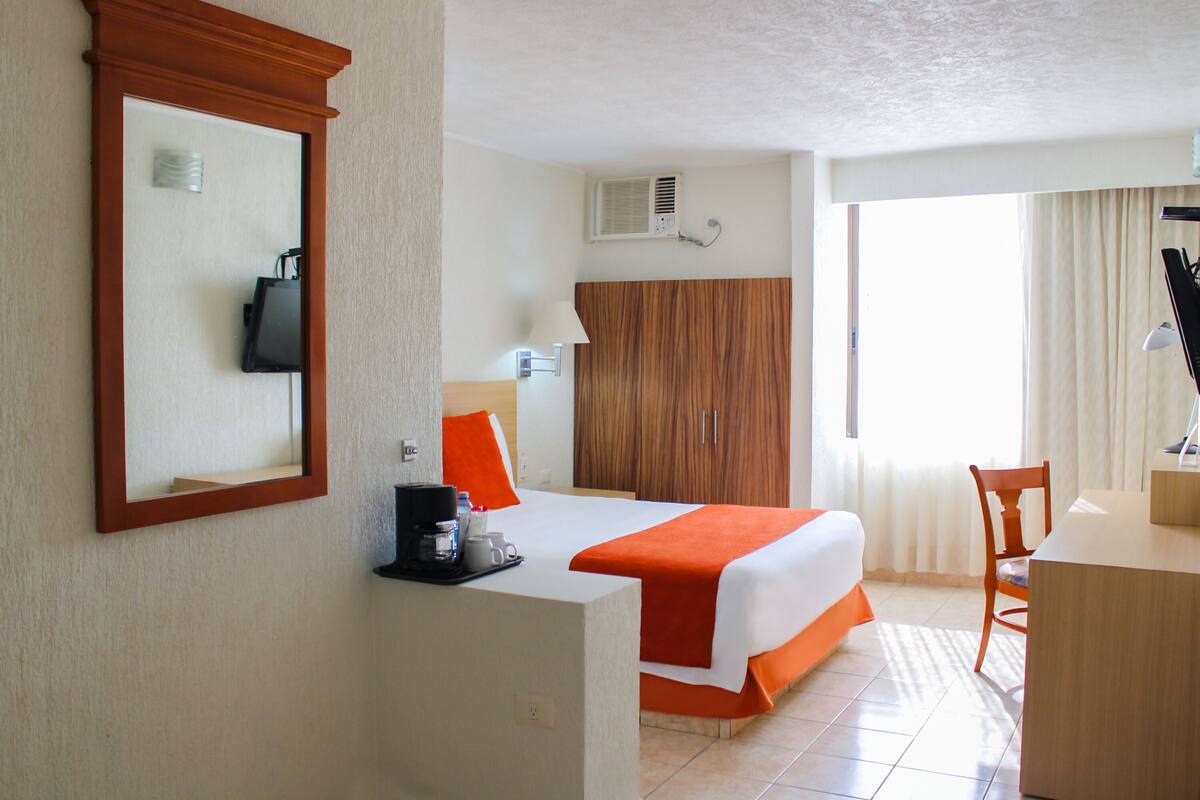 Une chambre d’hôtel équipée d’un lit, d’un bureau, d’une chaise, d’un miroir, d’une armoire et d’un appareil de climatisation.