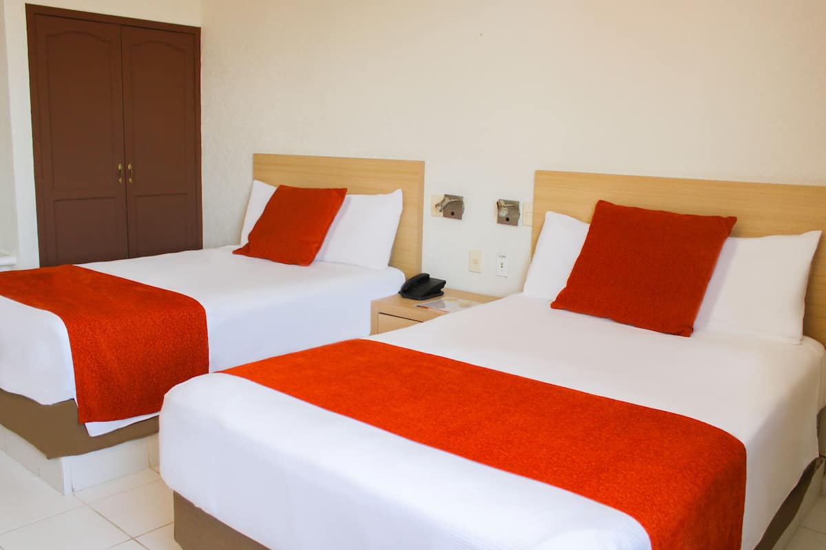 Deux lits simples avec des têtes de lit en bois, une literie blanche et des coussins décoratifs orange.