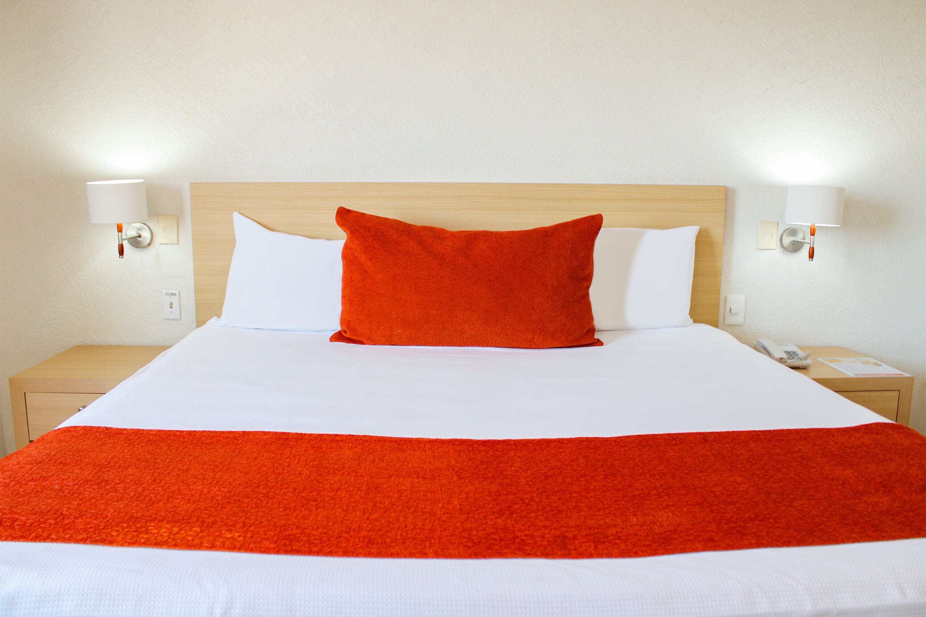 A hotel room with a large bed, white bedding, a wooden headboard, and two bedside lamps.