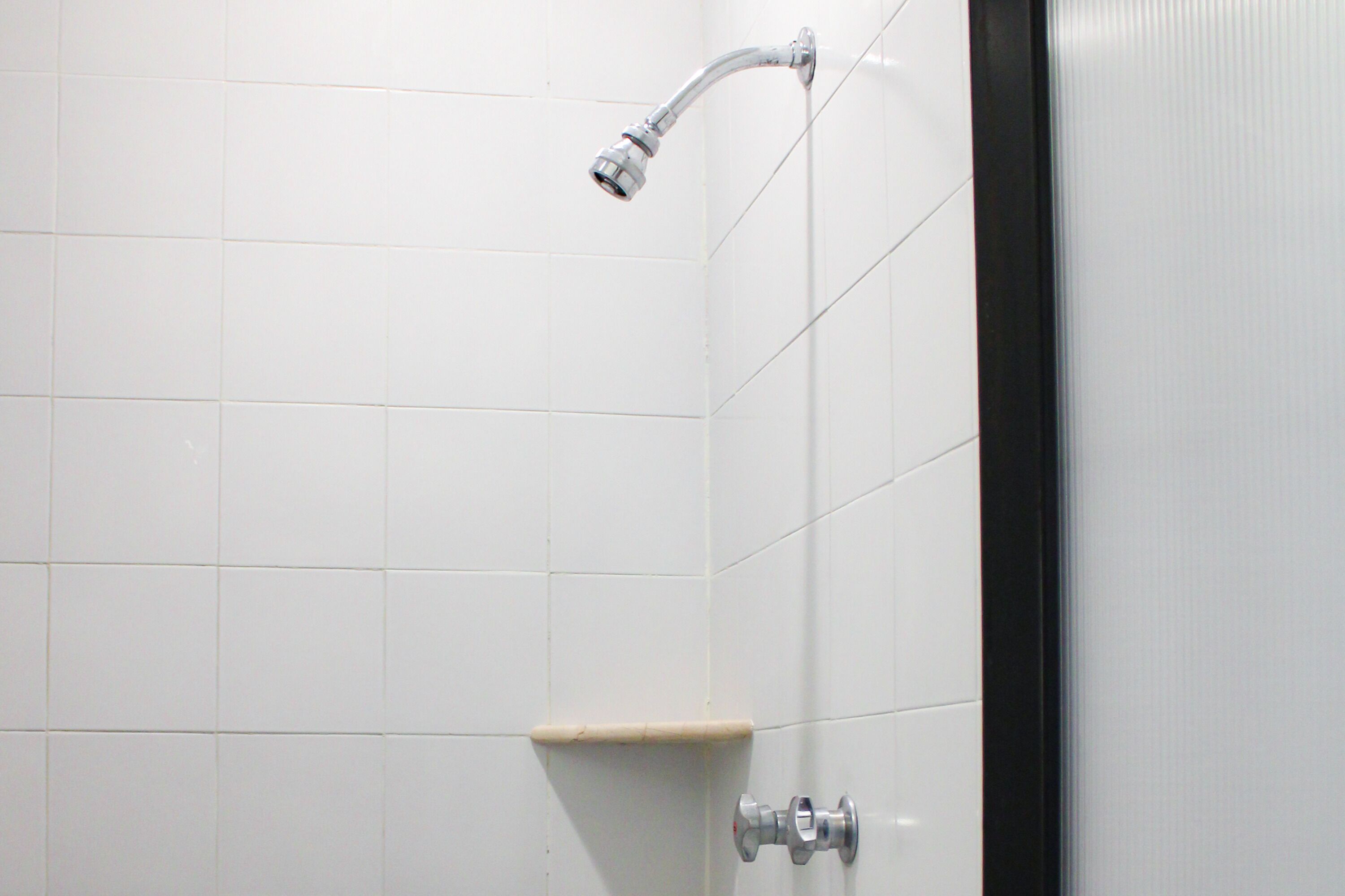 A bathroom with white tiled walls, a shower head, and a toilet.