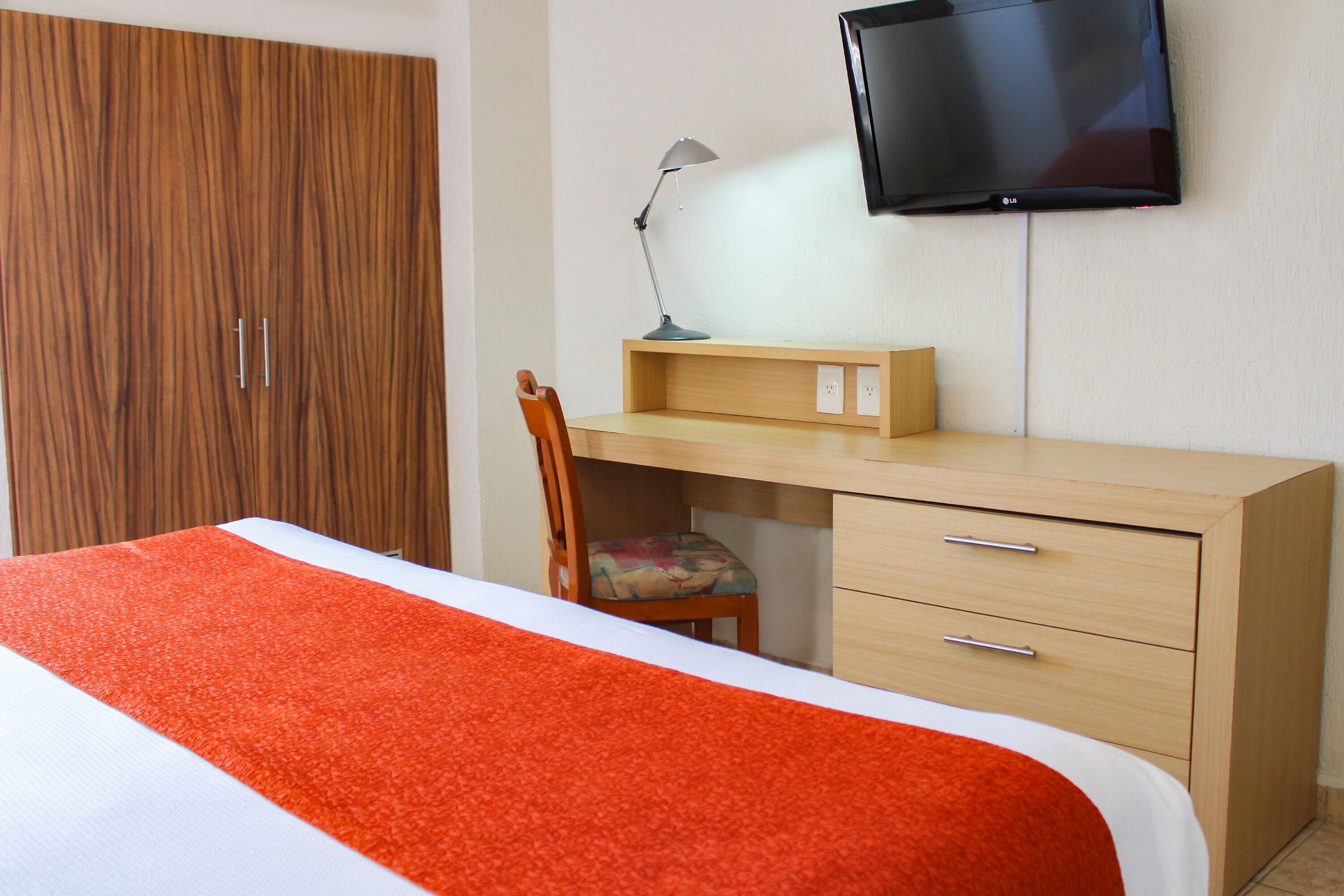 Une chambre d’hôtel comprenant un lit, un bureau avec une chaise, un téléviseur fixé au mur et une armoire.