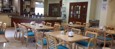 A dining area with wooden tables and chairs, a counter with a display, and a mirror above the counter.
