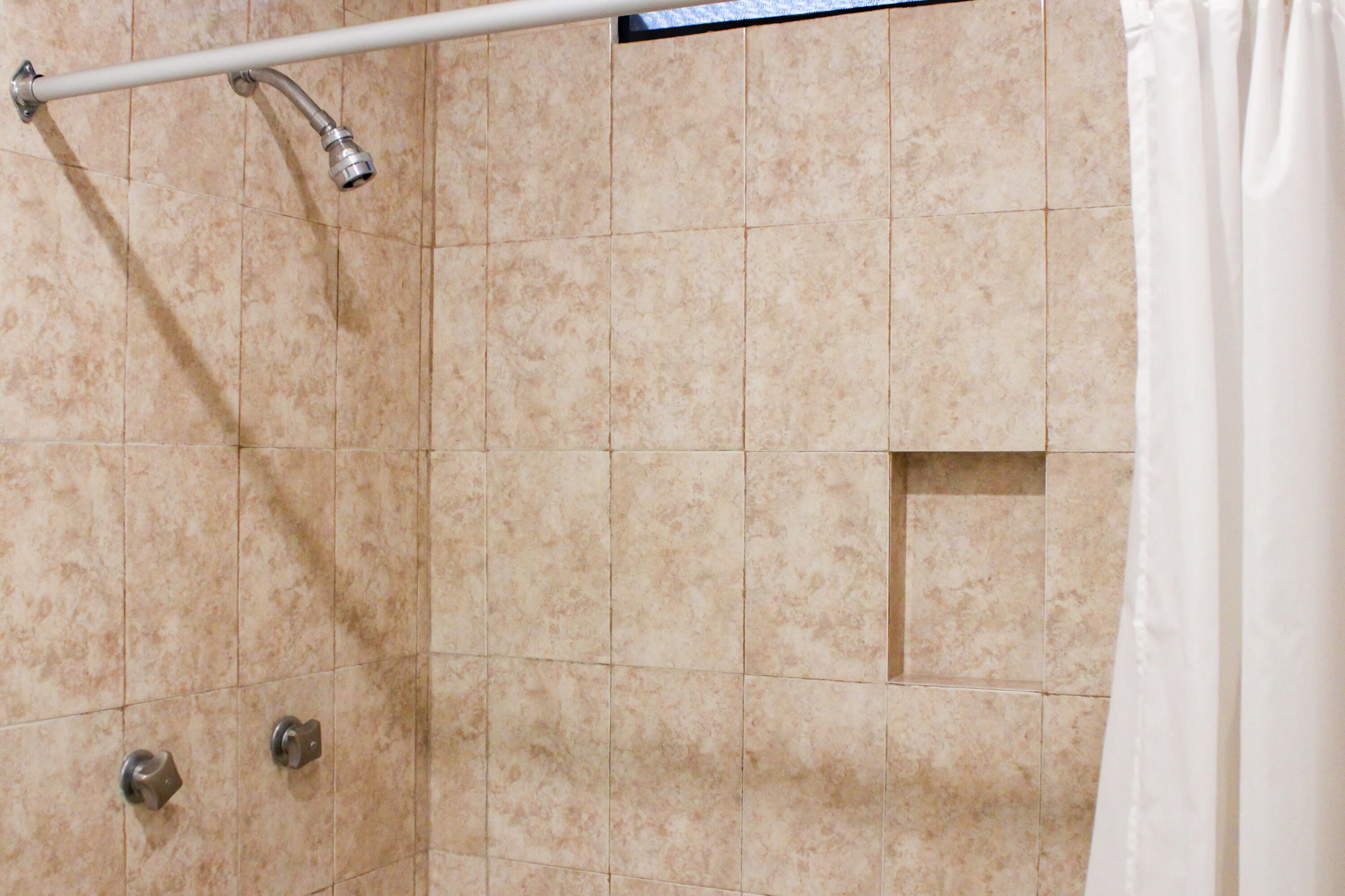 A tiled shower area with a white curtain, a metal showerhead, and a handrail.