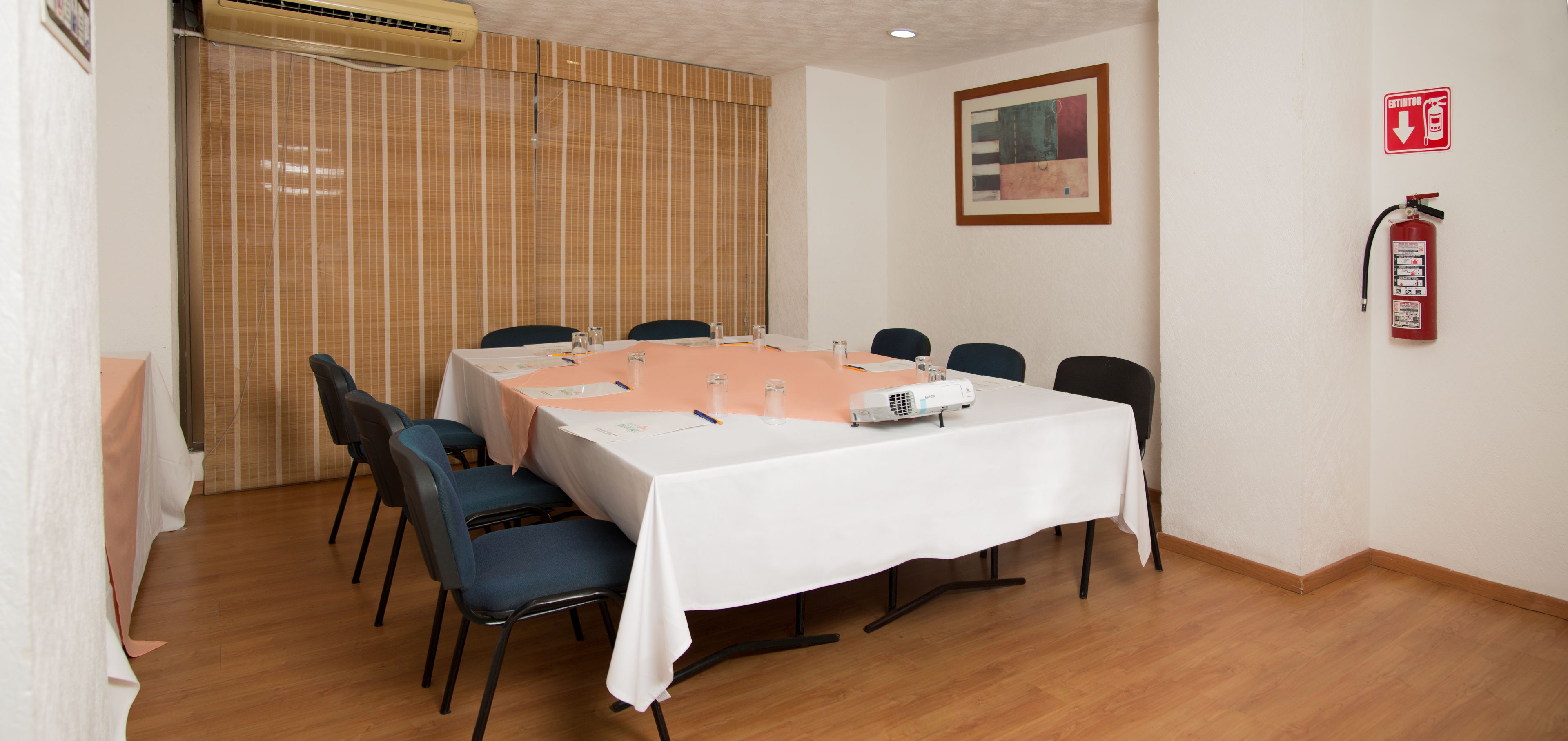 A conference room with a long table, chairs, a projector, and a fire extinguisher.