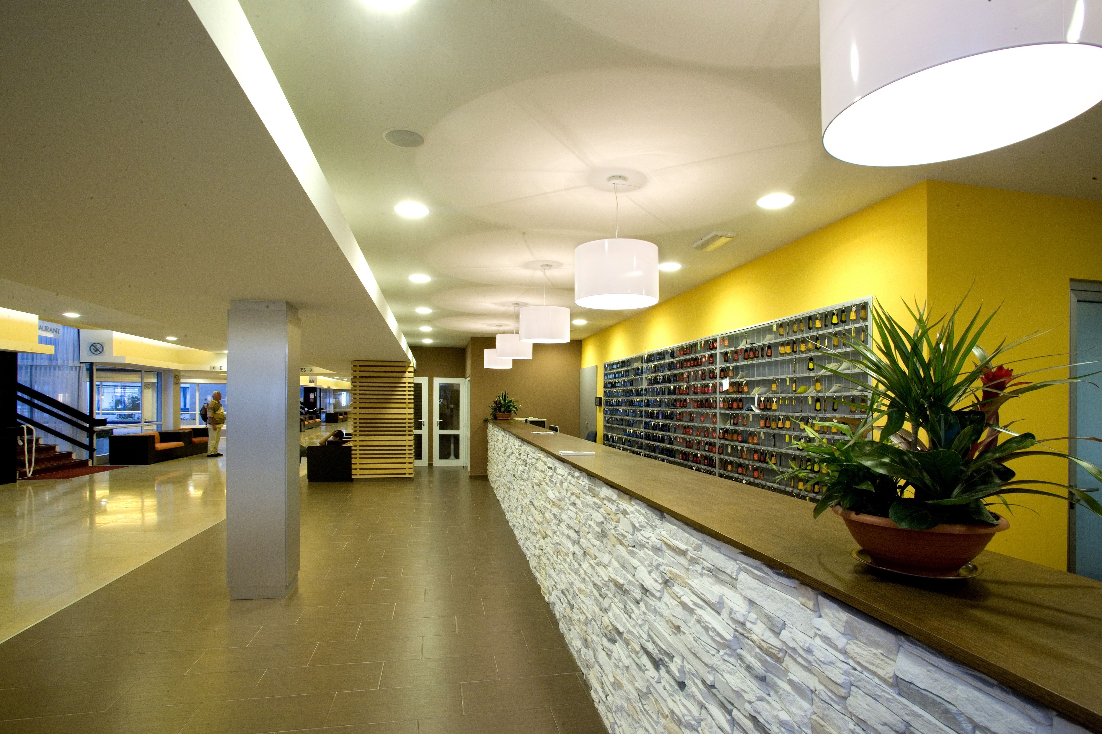 A hotel lobby with a reception desk, a wall of framed photos, and a staircase in the background.