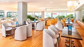 A modern restaurant with white and orange seating, wooden floors, and large windows offering a view of the sea. - Hotel Delfin Plava Laguna (Funtana)