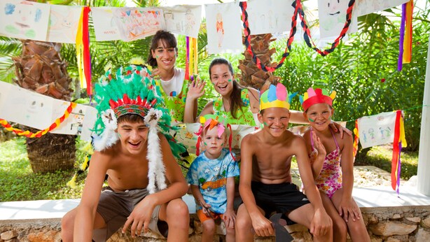 A group of people sitting on a stone bench outdoors, surrounded by greenery and decorated with colorful streamers. - Hotel Delfin Plava Laguna (Funtana)