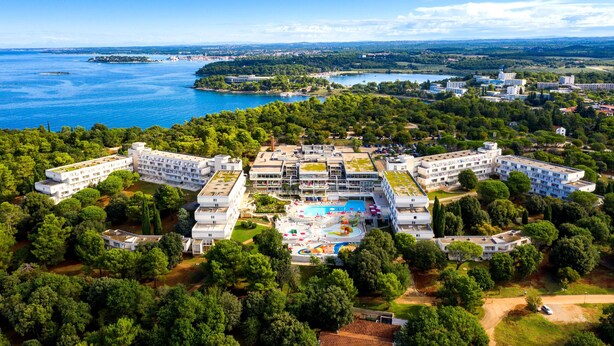 An aerial view of a hotel complex with multiple buildings, a central swimming pool, and surrounding greenery. - Hotel Delfin Plava Laguna (Funtana)