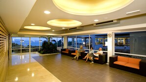 A spacious lobby with modern circular ceiling lights, comfortable seating areas, and large windows offering views of the outdoors. - Hotel Delfin Plava Laguna (Funtana)