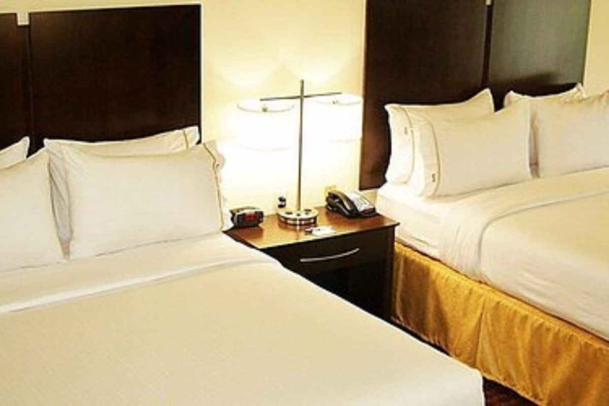 A hotel room with two beds, a nightstand with a lamp, and a telephone.