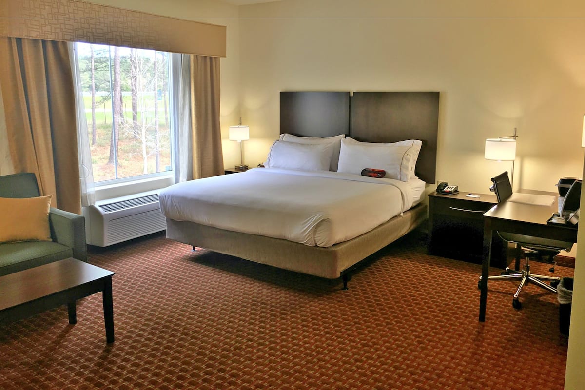 A hotel room with a large bed, two bedside tables with lamps, a desk, a chair, and a window with curtains.